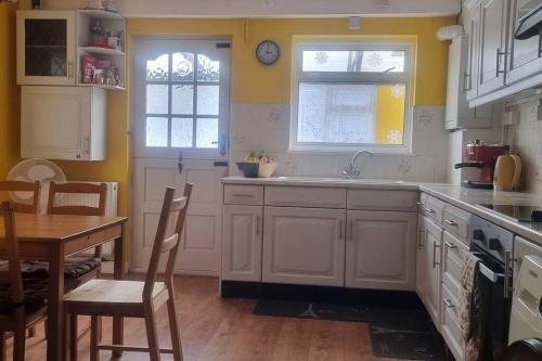 una cucina con armadi bianchi, tavolo e lavandino di Lovely 5-bed home with free parking and garden a Addington
