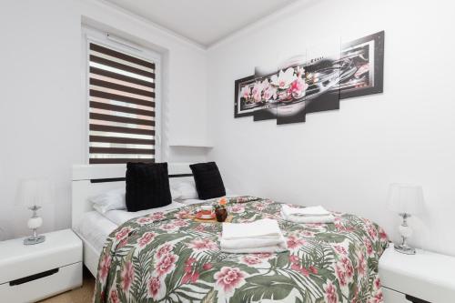 a white bedroom with a bed with a floral bedspread at Apartament Osiedle Bursztynowe Bałtycka by Renters in Kołobrzeg