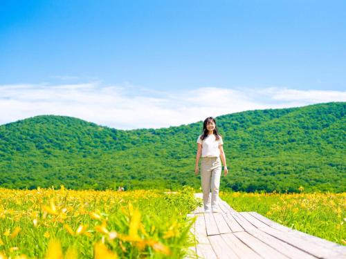a woman walking on a wooden path in a field at Urabandai Lake Resort Goshiki no Mori in Kitashiobara