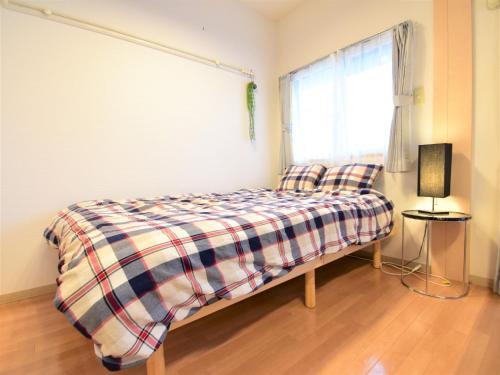 um quarto com uma cama com um cobertor xadrez e uma janela em Alphabed Fukuyama Nishi Sakura Machi 205 / Vacation STAY 22290 em Fukuyama