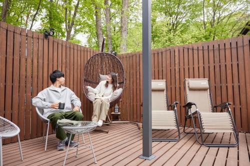 a man and woman sitting in a chair on a deck at サウナ・ジャグジー・完全貸し切りという贅沢　大人の秘密基地　Tiny Cabin TATEGU#02 in Miyota