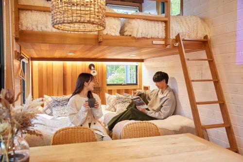 a man and woman sitting in a room with a bunk bed at サウナ・ジャグジー・完全貸し切りという贅沢　大人の秘密基地　Tiny Cabin TATEGU#02 in Miyota
