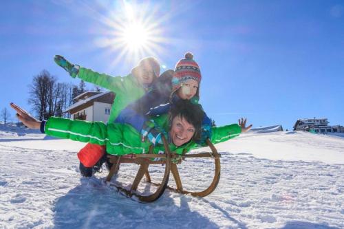 three children riding on a sled in the snow at Frühstückspension Bilgeri in Sulzberg