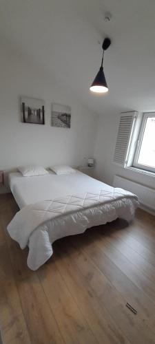 uma cama branca num quarto com piso em madeira em de blinker em Knokke-Heist