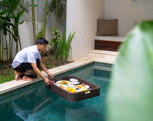 a man with a basket of food in a swimming pool at Tanadewa Villas & Spa in Nusa Dua