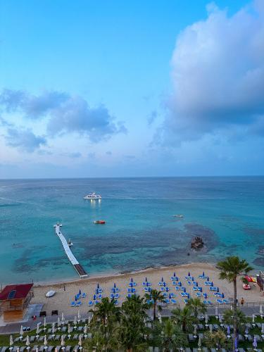a beach with blue chairs and a boat in the water at Silver Sands Beach Hotel in Protaras