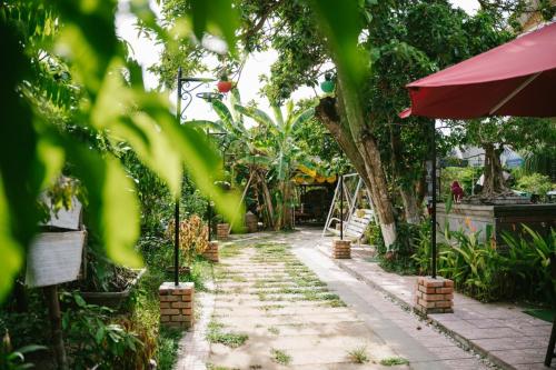 a garden path with trees and a red umbrella at Hue Lotus Homestay in Hue