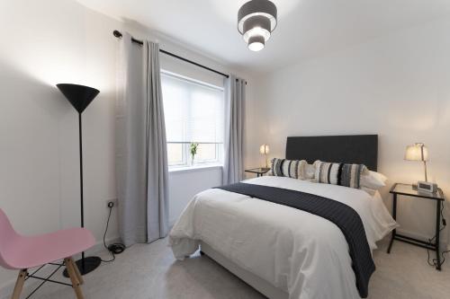 a white bedroom with a bed and a pink chair at Mhuilinn Apartment in Stirling