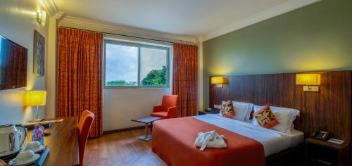 a hotel room with a bed and a chair and a window at Alisa Hotel North Ridge in Accra