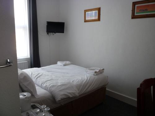 a bedroom with a bed with white sheets and a television at Bow Guest House in Reading