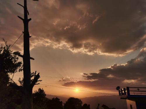 a sunset with a telephone pole in front of a hill at Sharda Stay's Binsar Himalayas in Almora