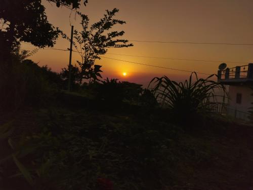 a sunset over a house with the sun in the sky at Sharda Stay's Binsar Himalayas in Almora