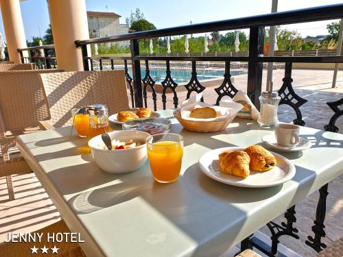 a table with breakfast food and orange juice on a balcony at Jenny Hotel in Laganas