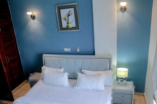 a blue bedroom with a bed with white sheets and pillows at Residence Le Carat Bonapriso in Douala