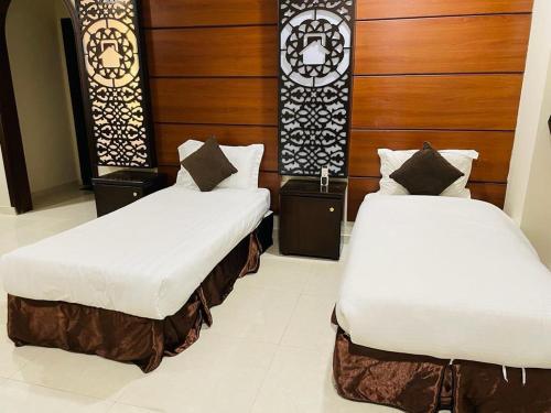 two beds in a room with white sheets and wood at Beat salsbil hotel in Al Madinah