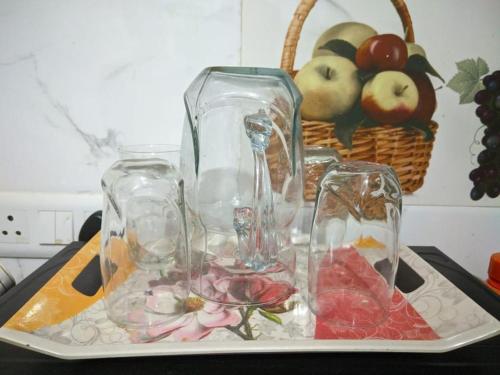 four glass vases on a tray with a basket of fruit at Kridha holidays homestay with kitchen in Vrindāvan