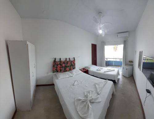 a white room with two beds and a window at Pousada Pé Na Areia in Arraial do Cabo