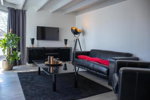 a living room with a black leather couch and a tv at Bed and Breakfast Harvey suite in Delden