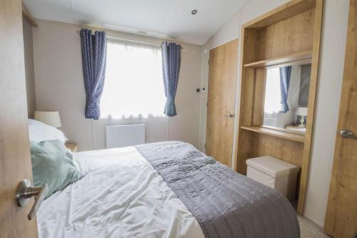 a bedroom with a bed and a window with blue curtains at Stunning Lodge Boasting Lake Views At Weely Bridge Holiday Park Ref 69005l in Weeley