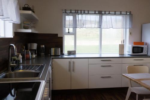 een keuken met witte kasten, een wastafel en een raam bij Guesthouse Helluland in Þingeyjarsveit