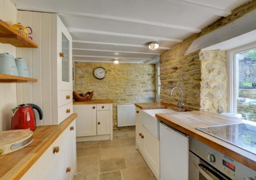 a kitchen with white cabinets and a stone wall at Little Steppes in Swanage