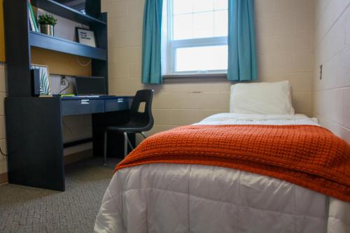 um quarto com uma cama, uma secretária e uma cadeira em Residence & Conference Centre - Timmins em Timmins