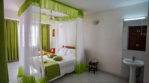Schlafzimmer mit einem Bett mit grünen Vorhängen und einem Waschbecken in der Unterkunft Hotel Windsor-Mombasa in Mombasa