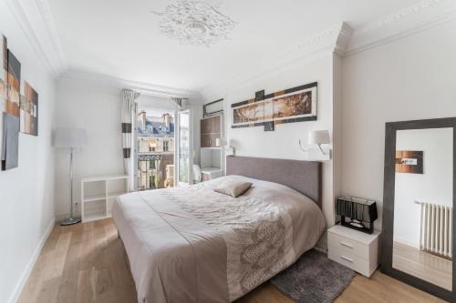 une chambre blanche avec un lit et un miroir dans l'établissement Appartement Haussmannien - dernier étage, à Paris