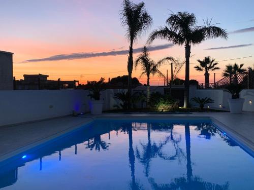 a swimming pool with palm trees and a sunset at Casa vacanze Misilla in Marsala