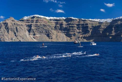 a group of boats in the water near a mountain at Pleasure Black Beach Perissa Santorini in Perissa