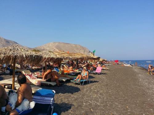 a crowd of people sitting on a beach with umbrellas at Pleasure Black Beach Perissa Santorini in Perissa