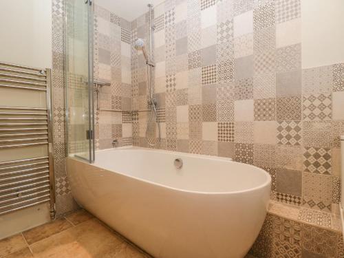 a white bath tub in a bathroom with tiles at The Hayloft in Honiton