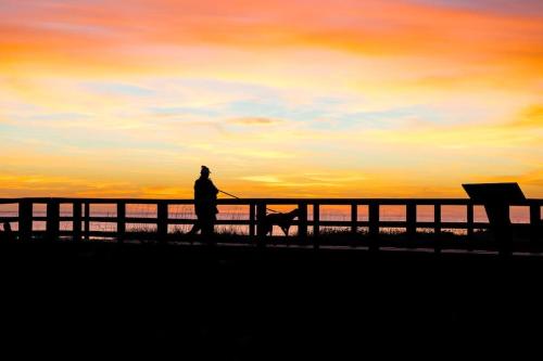 a man walking a dog on a pier at sunset at Anchor Haven Ocean Views in Oak Island