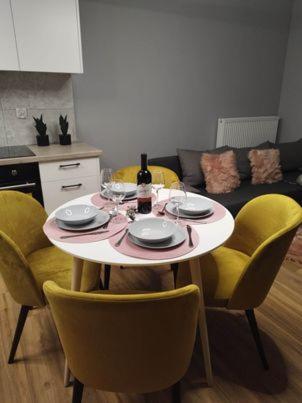 a dining room table with yellow chairs and a table with a wine bottle at Apartament Mińsk Mazowiecki in Mińsk Mazowiecki