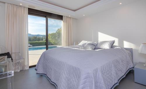 a white bedroom with a bed and a large window at 5 bed-villa with golf court view in Marbella