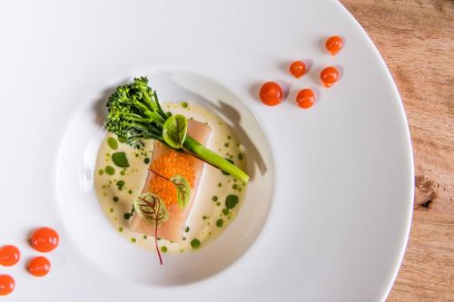 a white plate with a piece of fish and tomatoes at Naturhotel Lüsnerhof in Luson