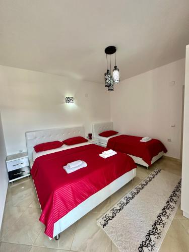 a bedroom with two beds with red sheets and a rug at Queen Kodre Apartments in Ulcinj