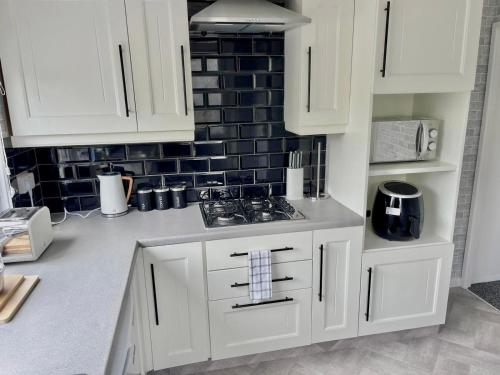 a kitchen with white cabinets and a black tile wall at Whittams Hot-tub Chalet Retreat in Heysham