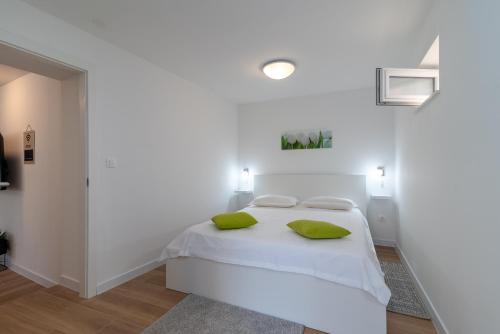 ein weißes Schlafzimmer mit einem weißen Bett mit grünen Kissen in der Unterkunft Apartman Benzon Vranjic in Vranjic