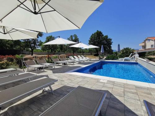 a swimming pool with chairs and umbrellas next to a pool at Apartments Lea with pool in Malinska