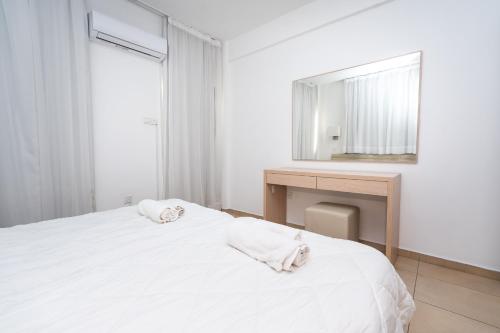 a white bedroom with a bed and a desk and a mirror at Flora Hotel Apartments in Protaras