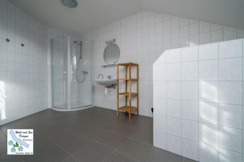 a white tiled bathroom with a sink and a shower at Wald und See Dargun 16B in Dargun
