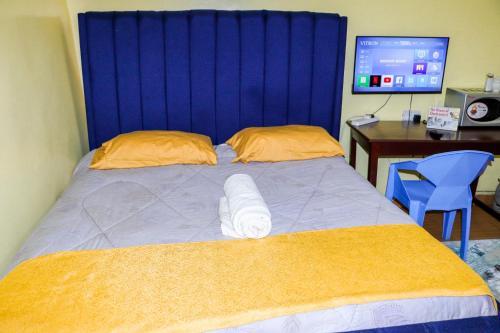 a bed with a blue headboard and a desk with a computer at Trendy Homes Studio BnB in Bungoma