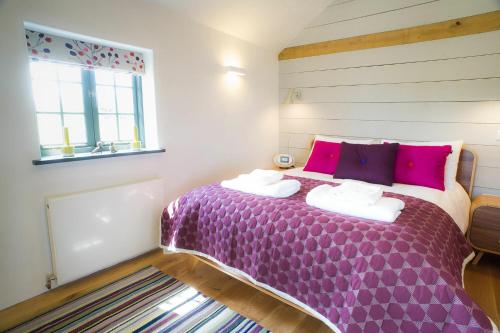 um quarto com uma cama roxa com almofadas cor-de-rosa e uma janela em The Seed Store, High Ash Farm em Peasenhall