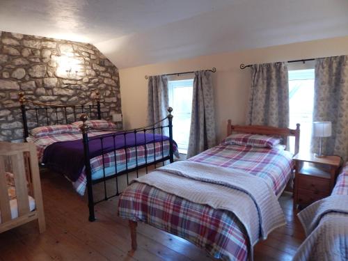 a bedroom with two beds and a stone wall at Burry Farm Cottage in Swansea