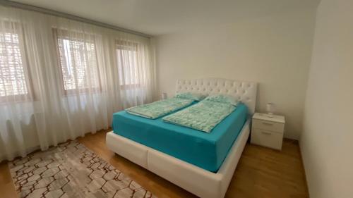 een slaapkamer met een bed met blauwe lakens en 2 ramen bij Stara Čaršija apartman in Sarajevo