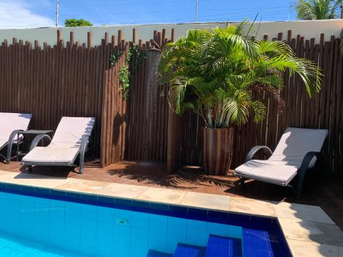 a pool with chairs and a palm tree next to a fence at Pousada Oasis Paracuru in Paracuru