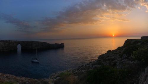 un barco en el agua con la puesta de sol en el fondo en Apart Calan Forcat Menorca, en Cala en Forcat