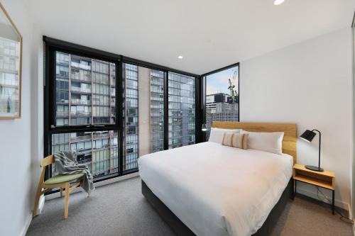 um quarto com uma grande cama branca e janelas grandes em The Canvas Apartment Hotel em Melbourne