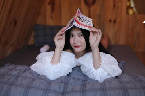 a woman is laying in bed with a book on her head at Trầm Homestay in Thôn An Hòa